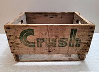 Front and side view of wooden CRUSH soda crate showing green logo and weathered wood surface.