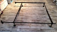 Complete adjustable metal bed rail frame assembled on wooden floor, showing rectangular shape and caster wheels.