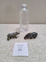Photo showing both antique cast metal rhino and hippo figurines side by side with a water bottle for size reference.
