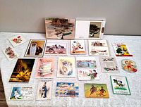 Wide layout showing all 19 vintage greeting cards and postcards arranged on a white fabric surface, exhibiting various colorful and vintage style designs with some featuring animals, people, and floral themes.