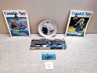 Overview of all items: two Canada’s Navy magazines, commemorative plate, model kit box, and USS John F Kennedy postcard.
