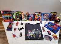 Full lot of Marvel and DC superhero toys, books, and Batman t-shirt laid out on floor