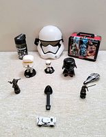 Full lot showing all items including a white Stormtrooper helmet, Star Wars water bottle, tin lunchbox, multiple bobblehead figures and small toys spread on the floor