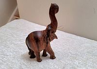 Side angle view of vintage wooden elephant carving with raised trunk and visible tusks