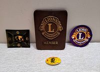 Four Lions Club International items displayed on white backdrop: member plaque, patch, ashtray, and button.