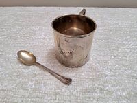 Vintage sterling silver baby cup engraved 'David' with accompanying Rogers silverplate spoon on a light textured background.