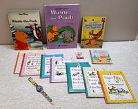 Full view of all eleven Winnie The Pooh books and children's watch laid out on a light cloth surface