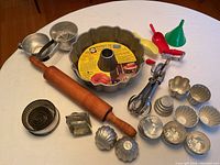 Overview of vintage baking molds, rolling pin, egg beater, funnels, cookie cutters, and flour sifter arranged on table