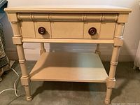 Frontal view of light wood side table with drawer and lower shelf, showing brass knobs.