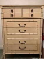 Front view of the beige tallboy dresser showing 8 drawers with bamboo design and solid brass handles.
