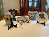 Overall view of ceramics and pottery items displayed on a table including plant pots, plates, a candle holder, small jar, and plate stands.