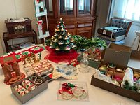 Wide view of tabletop with ceramic tree lamp, artificial garland, boxes of ornaments, textiles and decorative accessories