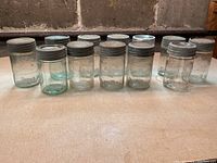 Front view of 12 Crown jars lined up, showing clear to aqua tint glass and lids