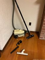 Side angle showing the Eureka Mighty Mite vacuum cleaner with hose and wand and all accessories laid out on wooden floor against wall.