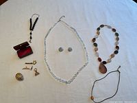 Full view of the lot showing necklaces, earrings, rosary beads, gold plated trinkets, and case, displayed on a flat surface.