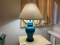 Full view of the blue ceramic lamp with cream pleated shade, showing size and style in room setting.