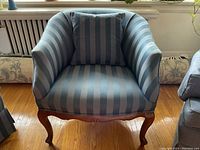 Front view of teal blue striped upholstered living room chair with carved wooden legs, showing matching pillow on the seat.