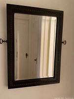 Front view of the beveled glass mirror with dark wood ornate frame and brass side handles.