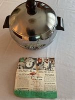 Closed view of the stainless steel Penguin Hot and Cold Server with black handles and lid knob, alongside instruction leaflet