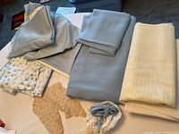 Overview showing several folded fabric pieces in light blue, beige, and floral pattern along with lace trim and binding on a white surface.
