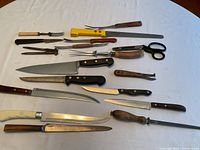 Full overhead view showing all utensils laid out on white cloth including carving knives, bread knives, fork, scissors, and sharpener.