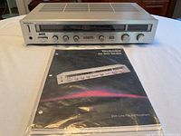 Front view of Technics SA-203 stereo receiver showing control panel and instruction manual in protective plastic sleeve.