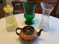 Lot showing four items on flat surface: a green glass vase, a clear glass vase, a plastic lemonade jug, and a ceramic tea pot.