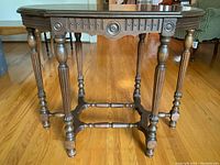 Full straight-on view of Victorian wall table showing six turned legs, carved apron with rosettes and groove details, and connecting struts on hardwood floor.