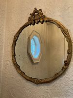 Full view of the vintage ornate round wall mirror hanging on textured wall near an octagonal window.
