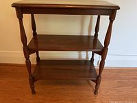 Front view of the wooden table showing three shelves and turned legs.