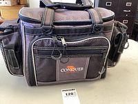 Front view of dark brown Conquer Outdoors fishing tackle bag with multiple zippered compartments and solid handles.