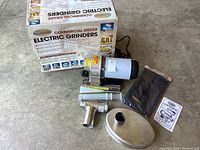 Overview of grinder unit, original box, pushers, cover bag, and manual on concrete floor