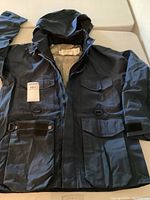 Front view of Cabela's navy rain jacket with hood and multiple pockets laid flat on a surface.