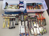 Overview of large collection of unopened crankbait lures and treble hooks in bins and laid out, showing variety of brands and models.