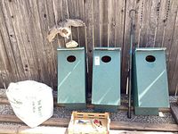 Three green wooden duck nesting boxes on bench with oval entrance holes, taxidermy mount on left box, bedding bag and tray of calls in front
