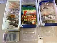Photo showing multiple resealable bags with assorted fishing worms and soft plastic baits inside white plastic storage containers.