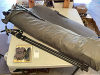 Large green Benelli-branded carrying case, two collapsible black support sticks, and packaged hunting accessory kit on white table.