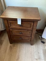 Front view of one bedside table showing three drawers with metal knobs and the Tuscan wood finish.
