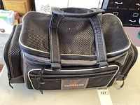 Black woven textured Conquer fishing tackle bag with multiple zippered compartments visible on table surface.