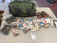 Full lot overview showing green carry bag, assorted fishing lures, hooks, and black Velcro straps on table.