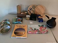 Overview of lot items arranged on table including abalone shells, candle, diffuser, paperweight, flags, cheeseboard and tools, wooden tray, and decorative vase.