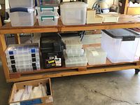 Wide shot showing various plastic storage containers on wooden shelving including latch compartment organizers, battery box, and large clear containers.