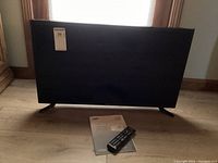 Front view of Samsung Series 5 32-inch LED TV standing with remote and manual in front on wood floor.