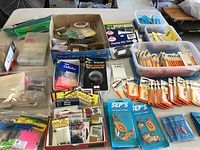 Wide view showing multiple plastic containers filled with various unopened fishing lures and accessories including Needlefish lures and tackle items.