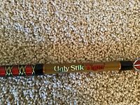Close-up of the Ugly Stik Tiger logo on the fishing rod, showing brown rod with decorative black and red wrappings.