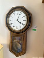 Front view showing wooden octagonal frame, white face with black Roman numerals, and pendulum in lower compartment with 'REGULATOR A' lettering on the glass door.