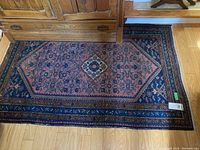 Full view of the Persian style carpet laid on wooden floor, showing the central medallion design, borders and general condition.
