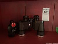 Photo showing vintage Bell & Howell binoculars with textured black body and silver trim control knobs.