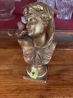 Bronze bust sculpture of a woman with a bird on her hand from front angle, showing detailed facial features and bird.