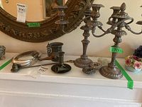 Wide view of all items on table showing candelabras, crumb catcher, snuffer, ornate cup and candle holder.
